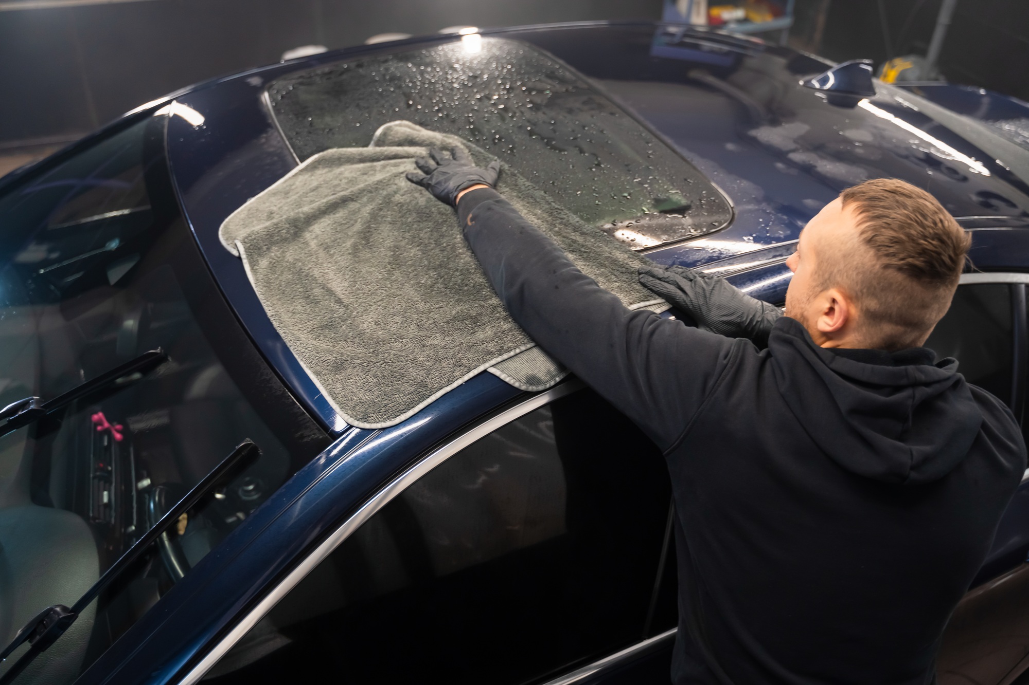 Ouvrier de lavage automobile de CleanCarByKev essuyant une voiture avec une serviette en microfibre après le lavage, service de nettoyage auto professionnel.
